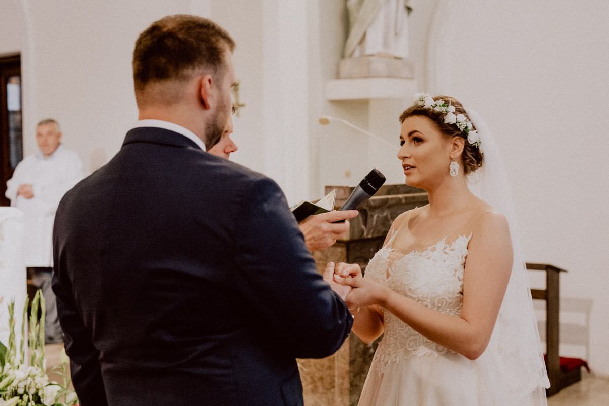 bride puts wedding ring on finger of groom