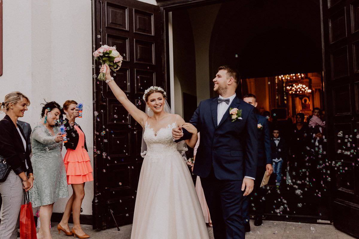 bride and groom goes out from the church, guests make bubbles in the air