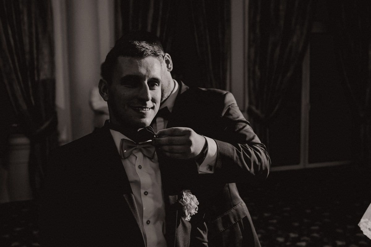 groom assumes witness bow tie around his neck